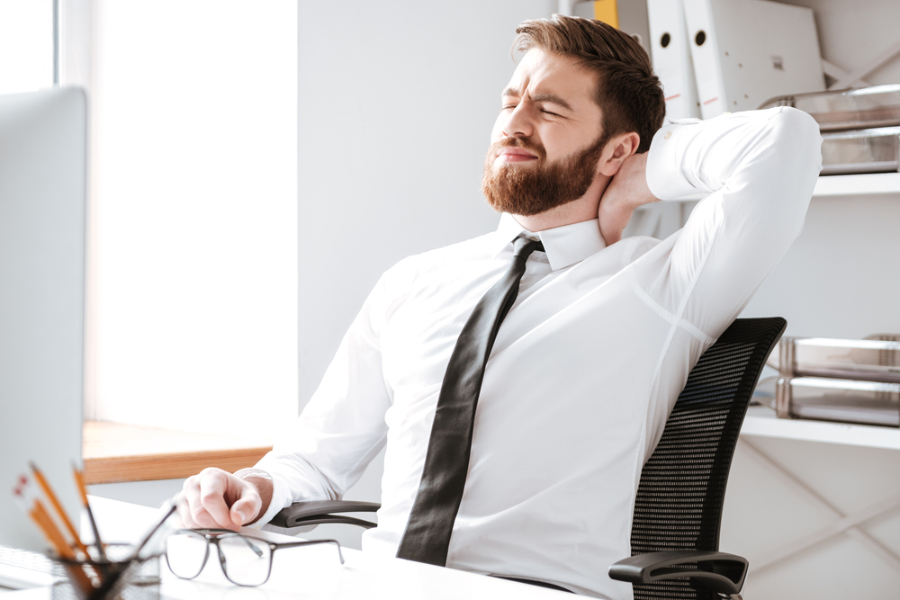 Photo of tired young businessman sitting in office while stretching