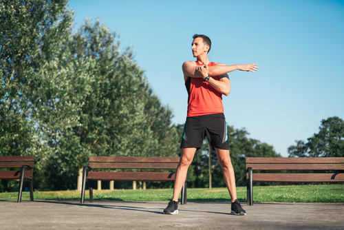 man doing shoulder stretch in park