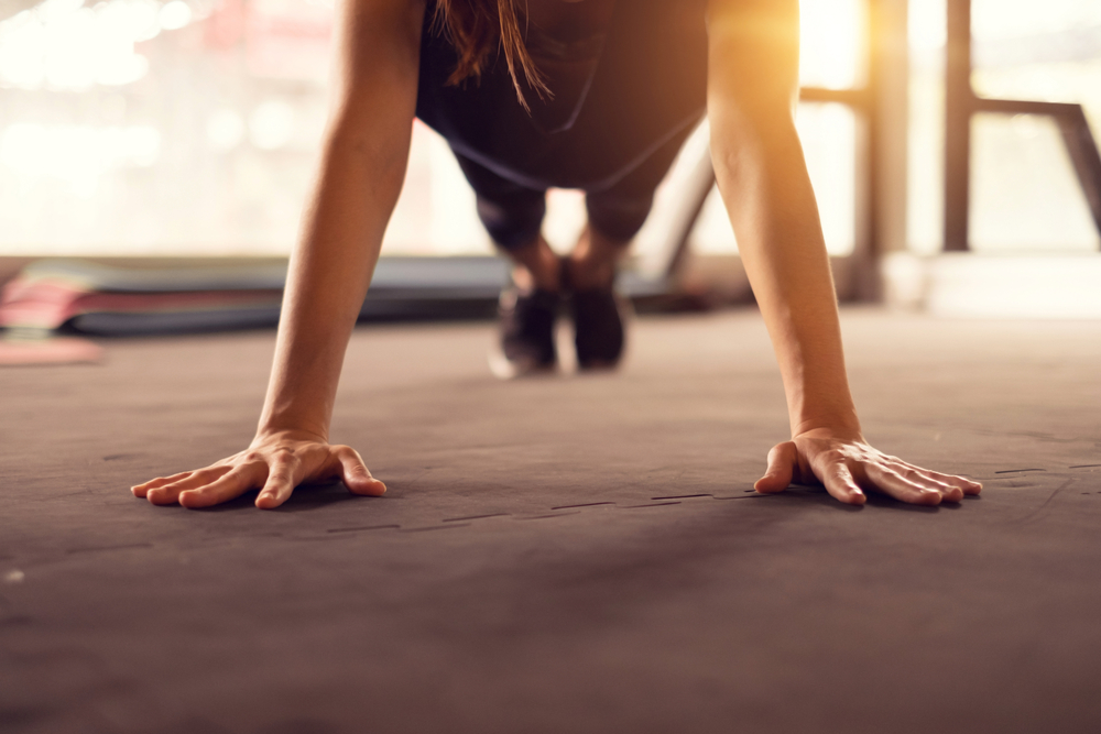 Close up woman hand doing push ups exercise in a gym in morning, sunlight effect.