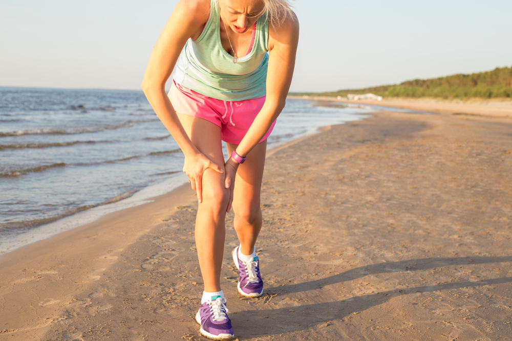 Woman on the beach holding her knee after running