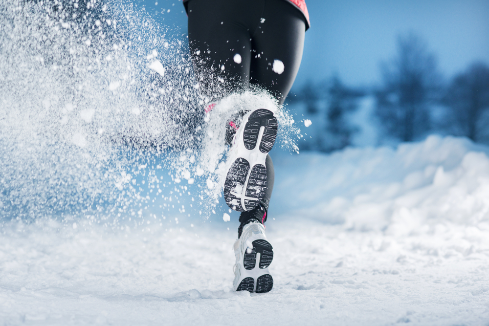 Athlete woman is running during winter training outside in cold snow weather.