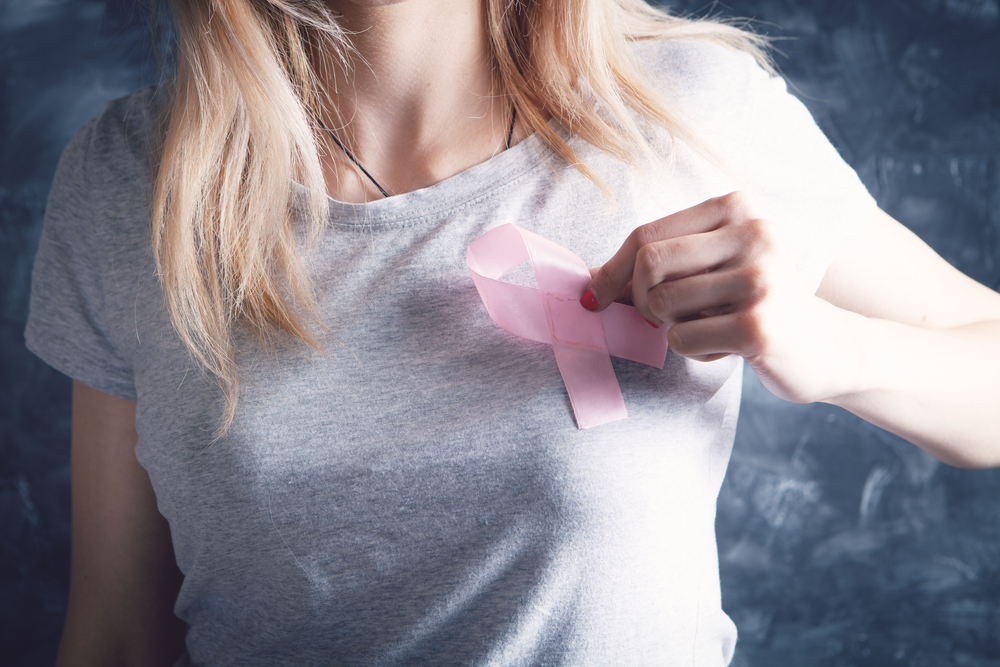 young woman holding pink ribbon near her chest on gray background