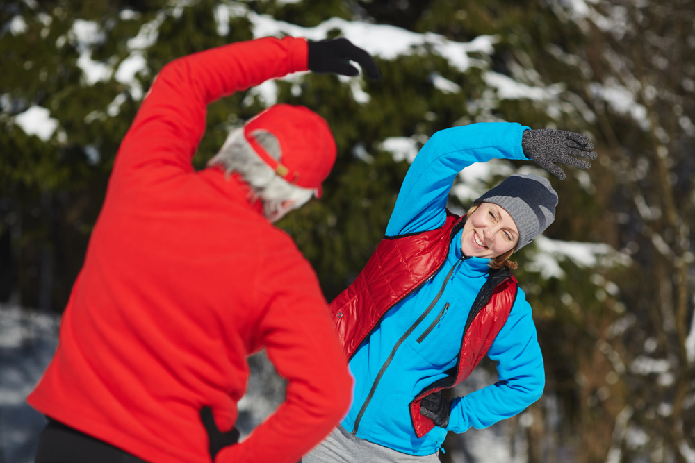 Happy mature woman in activewear standing in front of her husband while both doing side-bends